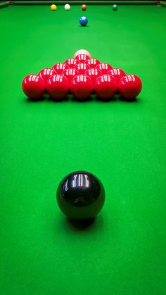 a pool table with red balls and green felt on the top, along with several black billards