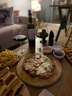 a table topped with pizza and french fries next to a bottle of wine on top of a wooden cutting board