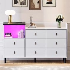 a white dresser with two pictures on the wall above it and a vase filled with flowers