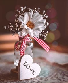 a vase filled with white flowers sitting on top of a wooden table next to a heart