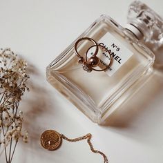 a bottle of chanel no 5 perfume next to a necklace and flower on a white surface