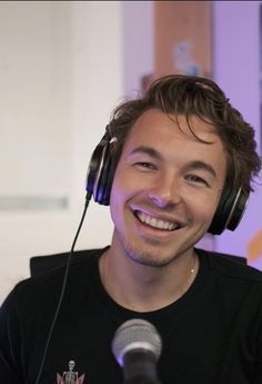 a man wearing headphones and smiling in front of a microphone