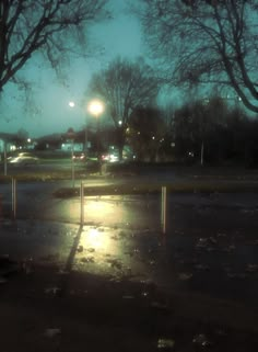 an empty parking lot at night with the lights on and trees in the foreground