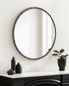 a round mirror sitting on top of a white table next to a potted plant