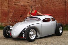 a woman sitting on top of a silver car in front of a brick building with a red roof