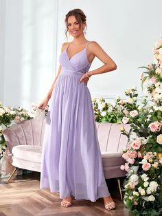 a woman in a long purple dress standing next to a couch and flower arrangement on the floor