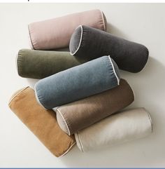 four different colored pillows stacked on top of each other in various sizes and colors, with one rolled up to the side