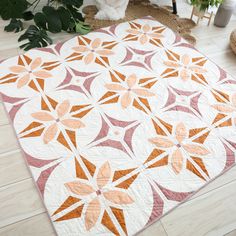 an orange and white quilt on the floor next to a potted plant in a living room