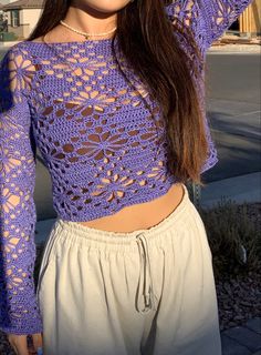 a woman wearing a purple crochet top and white pants is posing for the camera