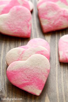 pink and white heart shaped cookies sitting on top of a wooden table next to each other