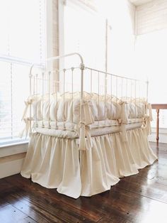 a white crib sitting on top of a hard wood floor next to a window