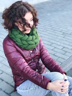 a woman sitting on the ground with her hands in her pockets and wearing a green scarf around her neck