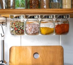 spices and seasonings in glass jars on a wooden shelf above a kitchen counter top