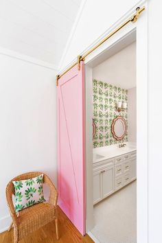 a pink door is opened to reveal a bathroom with white walls and wood flooring