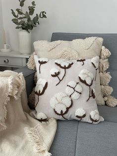 a gray couch with a white and brown pillow on top of it next to a plant