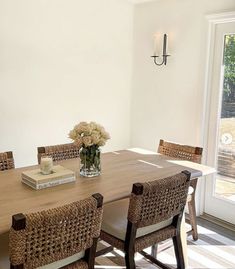 a dining room table with wicker chairs and flowers in a vase on the table