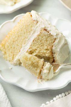 a slice of cake on a white plate with a fork next to it and another piece in the background