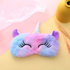 a sleeping mask with a unicorn horn on it next to a pink and blue pillow