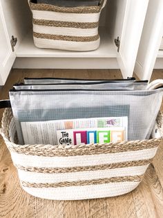 a white basket filled with magazines sitting on top of a wooden floor next to a cabinet