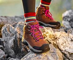 a person standing on top of a rock wearing brown boots and colorful socks with pink laces