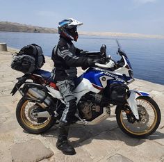 a man sitting on top of a motorcycle next to the ocean with his helmet on