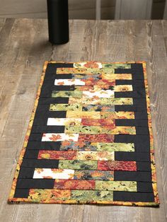 a black and yellow patchwork table runner on top of a wooden floor next to a vase