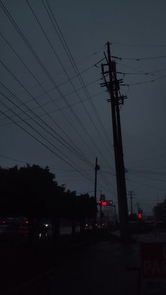 an electric pole with many wires above it at night, in the distance is a red traffic light