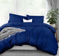 a blue comforter and pillows on a bed in a room with a plant next to the window