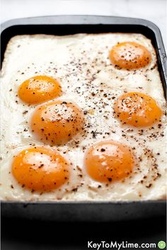 four fried eggs in a pan with seasoning sprinkled on top, ready to be eaten