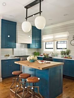 a kitchen with blue cabinets and stools in front of an island that has three lights hanging from the ceiling