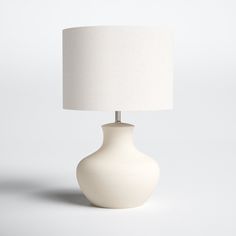 a white table lamp with a white shade on the base and a light bulb attached to it