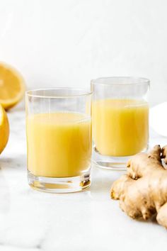 two glasses filled with orange juice next to sliced lemons and ginger on a table