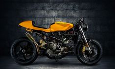 a yellow and black motorcycle is parked in a dark room with concrete walls behind it