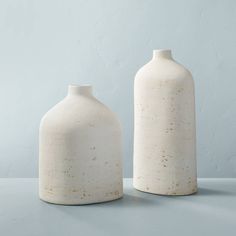 two white vases sitting next to each other on top of a gray countertop