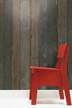 a red chair sitting in front of a wooden wall with planks on it's sides