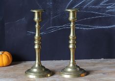 two gold candlesticks sitting on top of a wooden table next to a pumpkin