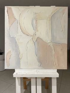 an abstract painting sitting on top of a white bench in front of a tiled floor