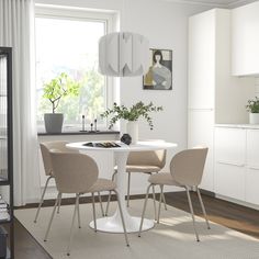 a white table with four chairs around it in front of a window and potted plant