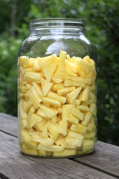 a mason jar filled with cut up pineapples sitting on a wooden table in front of some trees