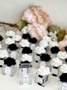 small clear boxes with black and white flowers in them sitting on a table next to a bouquet of roses