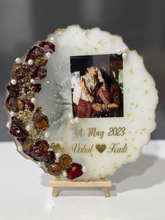 a white and gold photo frame with beads around it on a wooden stand next to a wall