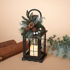 a candle is lit in a lantern with greenery and pine cones