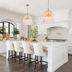 a large kitchen with white cabinets and marble counter tops, along with bar stools that match the hardwood flooring