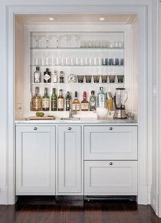 a white kitchen with lots of bottles and glasses on the shelves above the bar area