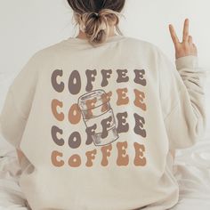 a woman sitting on top of a bed wearing a sweatshirt that says coffee and coffee