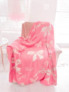 a pink blanket sitting on top of a chair next to a white table and window