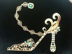 a tiara and brooch are laying on a black velvet surface, one has a green stone in the center