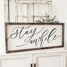 a wooden sign that says stay awhile on top of a white cabinet next to a potted plant