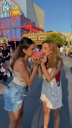 two young women sharing a piece of cake in front of an amusement park ride area