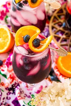 two glasses filled with blueberry lemonade and orange slices on top of a floral table cloth